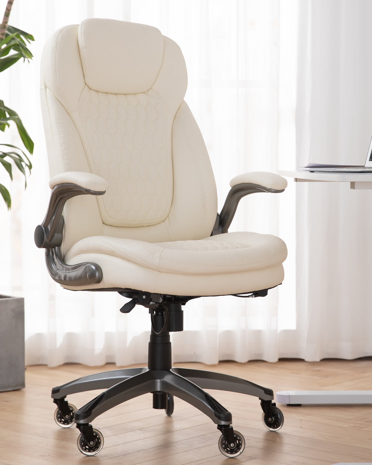 An ivory leather executive office chair in a bright room, beside a plant and a desk.